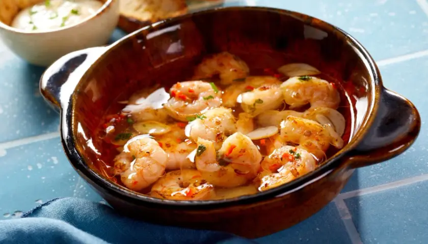 En skål med saftiga gambas pil pil, simmande i vitlök och chiliolja, redo att avnjutas med rostat bröd.