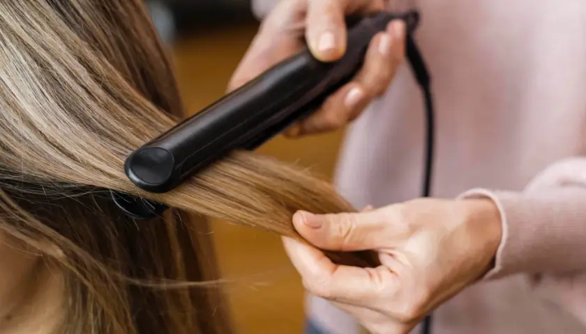 Hårstylist rätar ut frissigt hår uppe på huvudet med ett plattång.