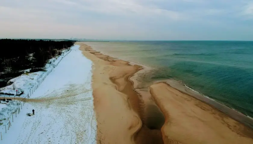 Plaża nad Bałtykiem zimą: śnieg, piasek i turkusowa woda.