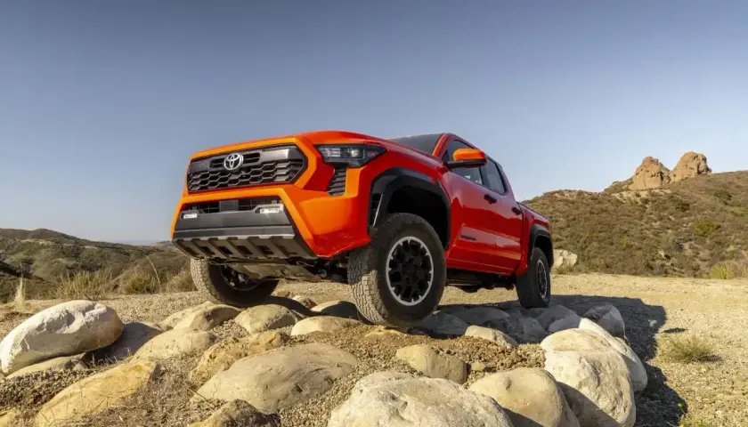 Pomarańczowa Toyota Tacoma pokonuje skalisty teren, gotowa na każdą przygodę.