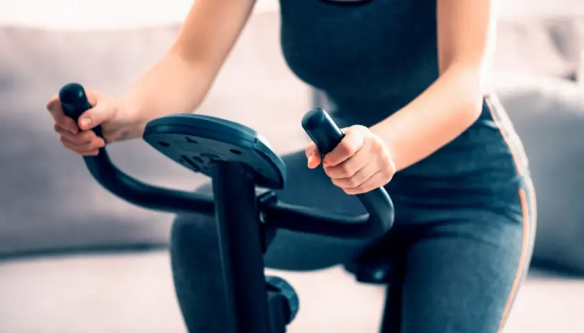 Kobieta wykonuje trening na rowerze stacjonarnym, trzymając kierownicę.