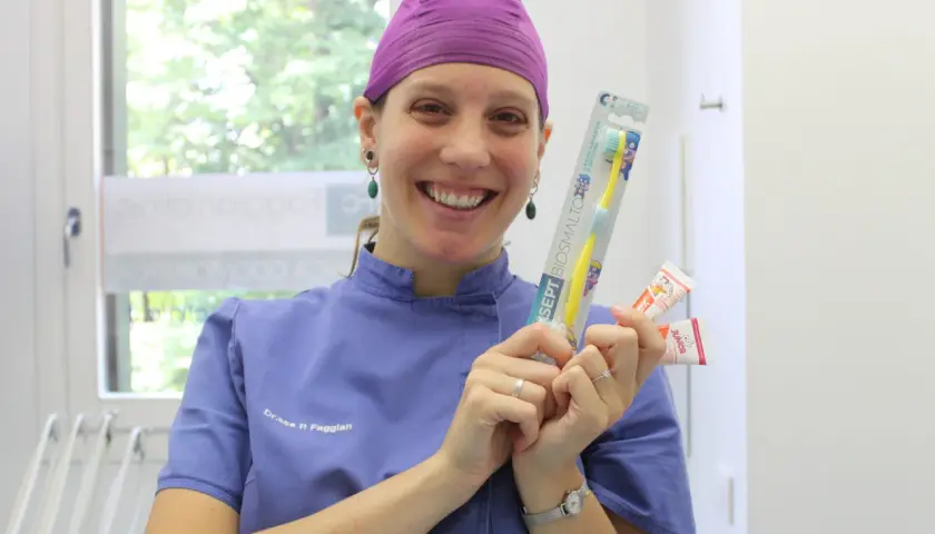 Sorriso di un dentista che mostra spazzolino e dentifrici per la pulizia dei denti bambini.