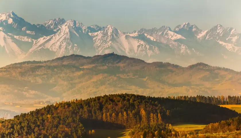 Majestatyczne karpackie szczyty ośnieżone, w dole jesienne wzgórza i lasy.