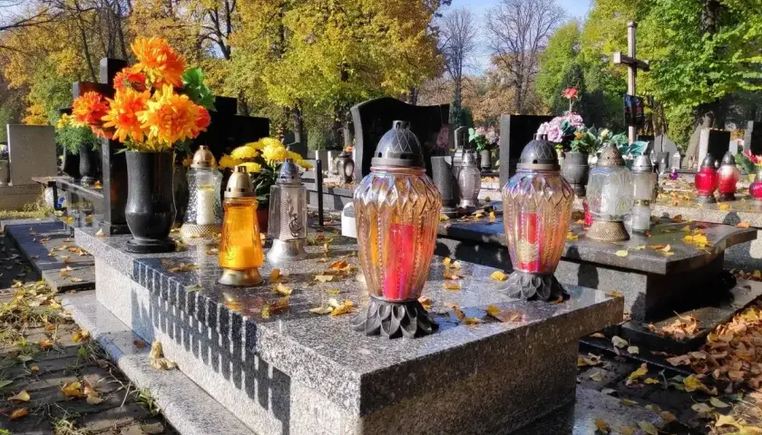 Jesienne miejsce na cmentarzu. Znicze i kwiaty na grobach, opadłe liście tworzą melancholijny nastrój.