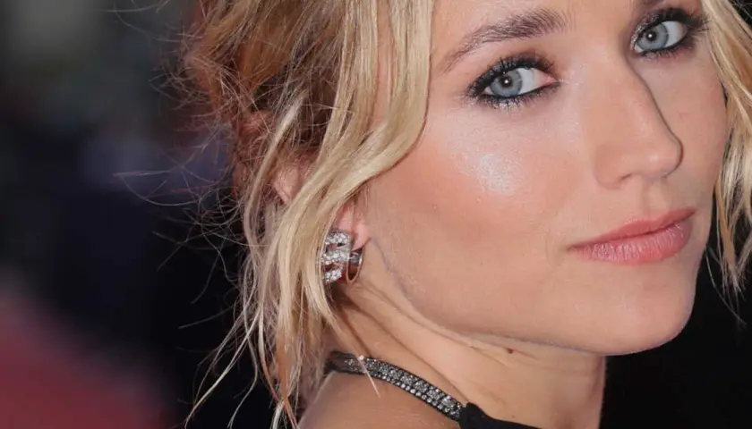 Maquillage yeux bleus d'une blonde, avec des boucles d'oreilles scintillantes et un collier discret.