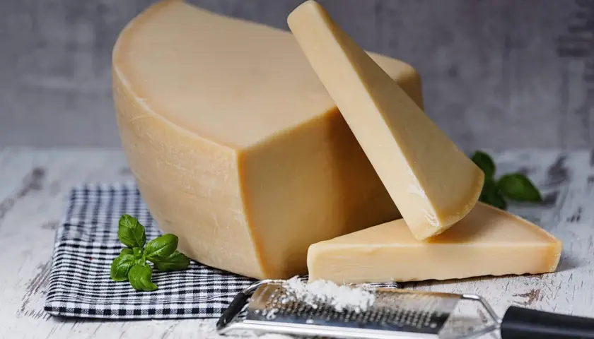 Twardy, żółty ser, przypominający parmezan- polski odpowiednik, leży obok tarki z wiórkami.