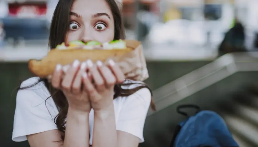 Zaskoczona dziewczyna trzyma duży kebab, zastanawiając się, ile kosztuje.