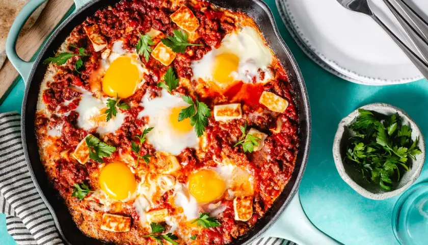 Chakchouka sans poivron : œufs pochés dans une sauce tomate épicée, parsemée de fromage halloumi grillé et de persil frais.