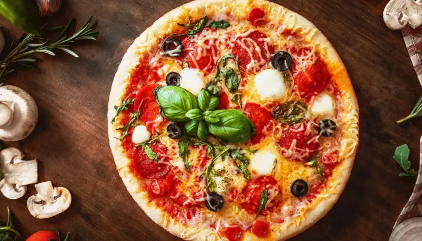 Leckere Pizza mit Salami, Mozzarella und Oliven auf einem Holzbrett. Ein schneller Pizzateig ohne Hefe macht sie im Handumdrehen fertig.