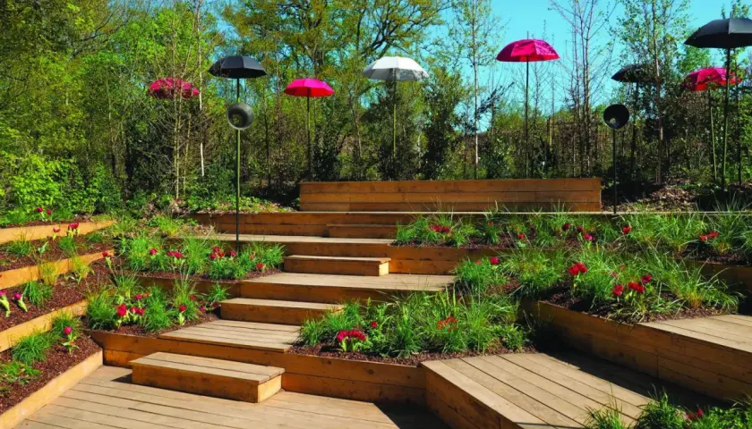Aménagement d'une butte de terre en pente avec des terrasses en bois, des tulipes rouges et des parasols colorés.
