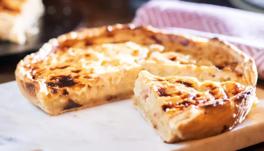 Ein köstliches Quiche Rezept, goldbraun gebacken, mit einem Stück zum Probieren.