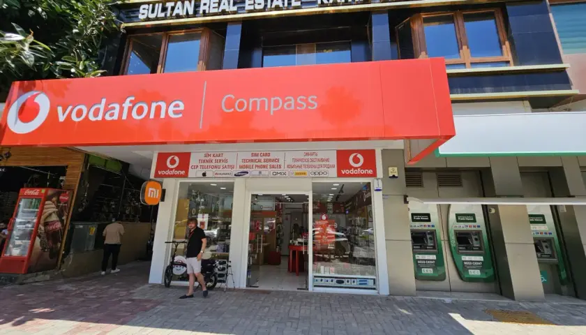 Sklep Vodafone z szyldem "Compass", bankomaty i lodówka Coca-Cola.