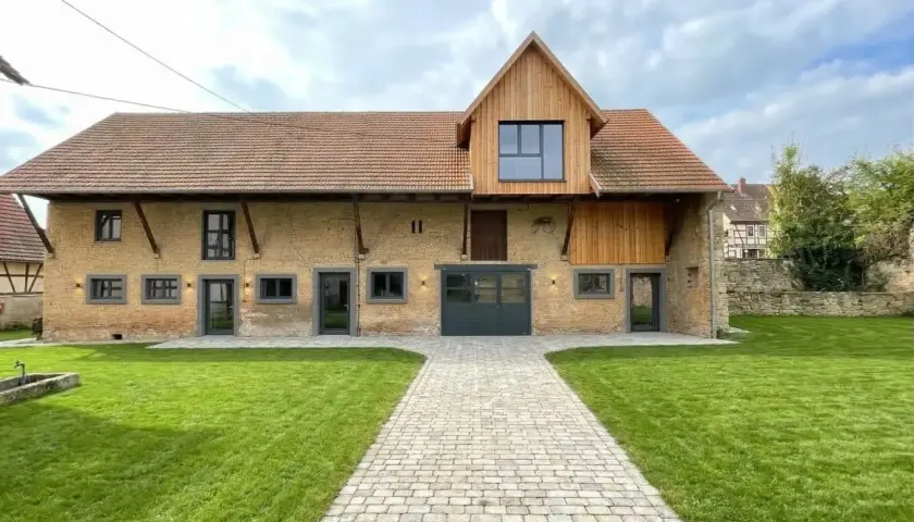 Magnifique grange transformée en habitation moderne, avec une extension en bois et de grandes fenêtres. Un exemple réussi de changement de destination.