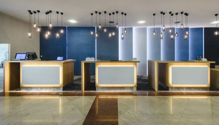 Recepcja hotelowa z trzema ladami, nowoczesnymi lampami i podświetlanymi panelami.