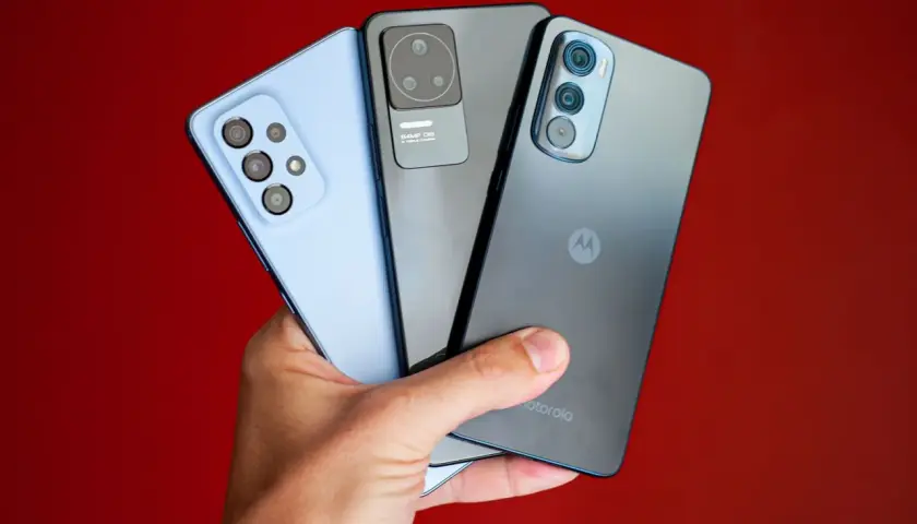 Dłoń trzyma trzy smartfony: jasnoniebieski, szary i ciemnoszary z logo Motorola. Kraj pochodzenia tej marki to USA.