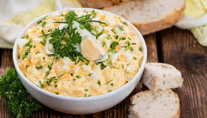 Pyszna pasta z jajek, udekorowana natką pietruszki i jajkiem na twardo, podana z chlebem.
