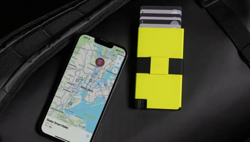 Ein Smartphone mit Karte von New York und ein gelbes Kartenetui liegen neben einem schwarzen Rucksack. Perfekt, um bargeldlos zu bezahlen.