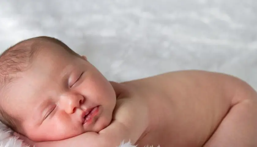 Śpiące, 3 miesięczne dziecko z delikatnymi włoskami, wtulone w miękkie futerko.