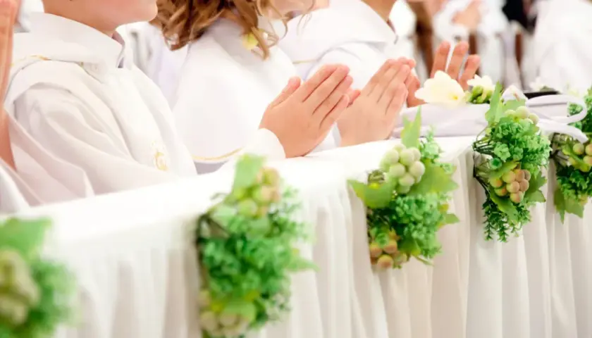 Dzieci w bieli, z modlącymi się dłońmi, czekają na komunię. Dekoracje z winogron i zieleni podkreślają uroczystość, a koszty komunii w kościele są nieodłącznym elementem tego dnia.