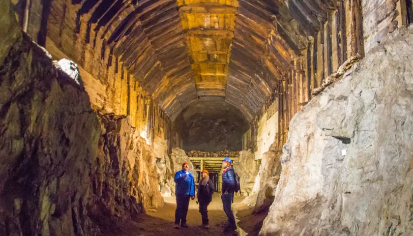 Trzech turystów z latarkami eksploruje mroczny tunel kopalni. Czy to osówka czy włodarz, trudno stwierdzić w tym labiryncie.