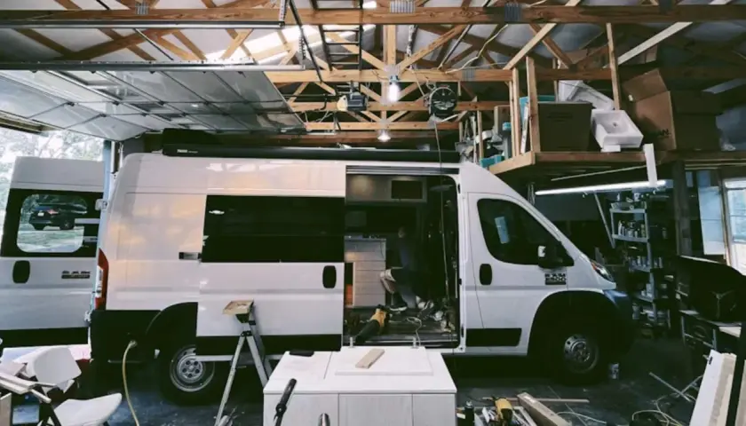 Aménagement d'un camion en cours dans un garage. Un homme travaille à l'intérieur, entouré d'outils et de matériaux.