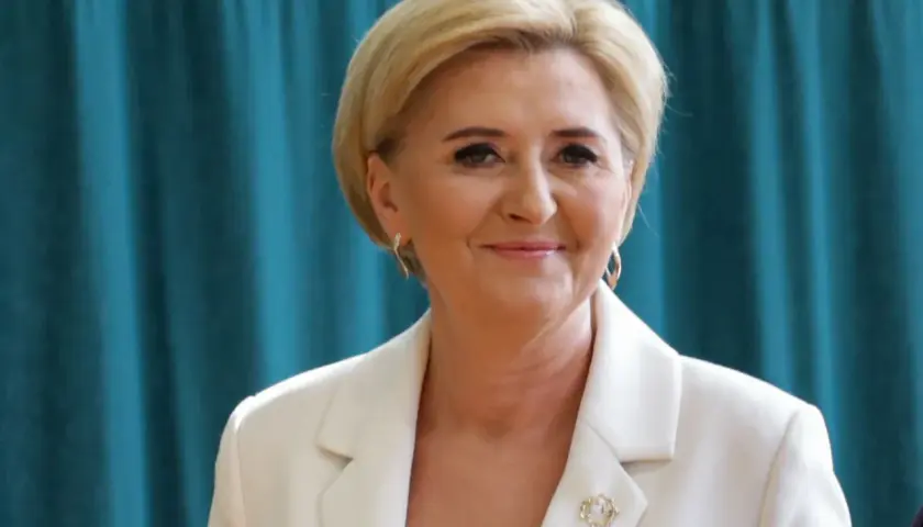 Uśmiechnięta kobieta w białej marynarce, z blond włosami i złotymi kolczykami. Czy żona prezydenta może pracować? Tak, jak najbardziej!