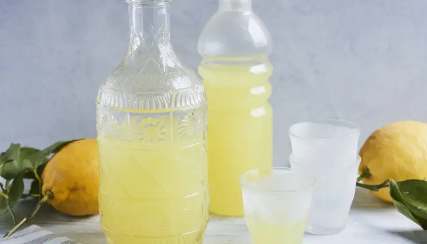 Ein Glas mit dem original italienischen Limoncello Rezept, daneben eine Karaffe, Flasche und Zitronen.