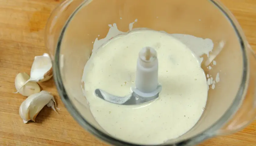 Crème d'ail onctueuse dans un mixeur, prête à être dégustée. Quelques gousses d'ail frais à côté.