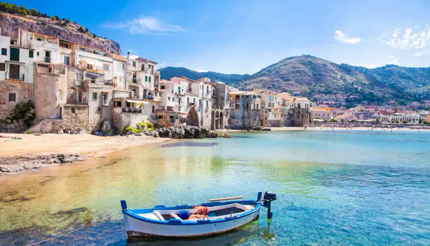 Barca a remi in acque cristalline davanti a Cefalù, con le sue case colorate e le spiagge più belle che invitano al relax.
