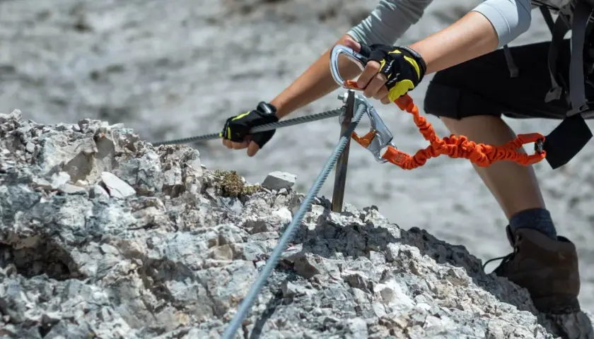 Ręce w rękawiczkach z karabinkami zabezpieczają się na stalowej linie podczas wspinaczki. To przygoda na via ferrata Słowacja.