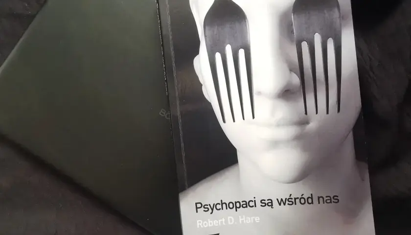 Okładka książki "Psychopaci są wśród nas" z widelcami zamiast oczu na twarzy.