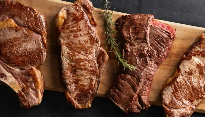 Quatre types de viande rouge grillée, dont un côte de bœuf, sont présentés sur une planche en bois.