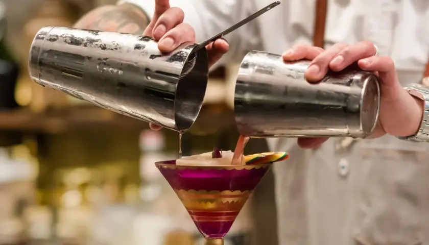 Barman przelewa drinka z shakera do drinków do ozdobnego kieliszka.