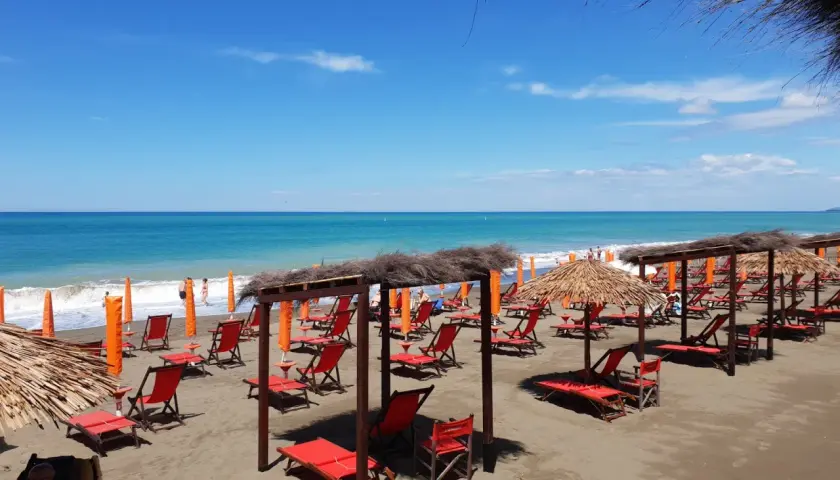 Plage de Marina di Bibbona avec des chaises longues rouges et des parasols de paille sous un ciel bleu éclatant.