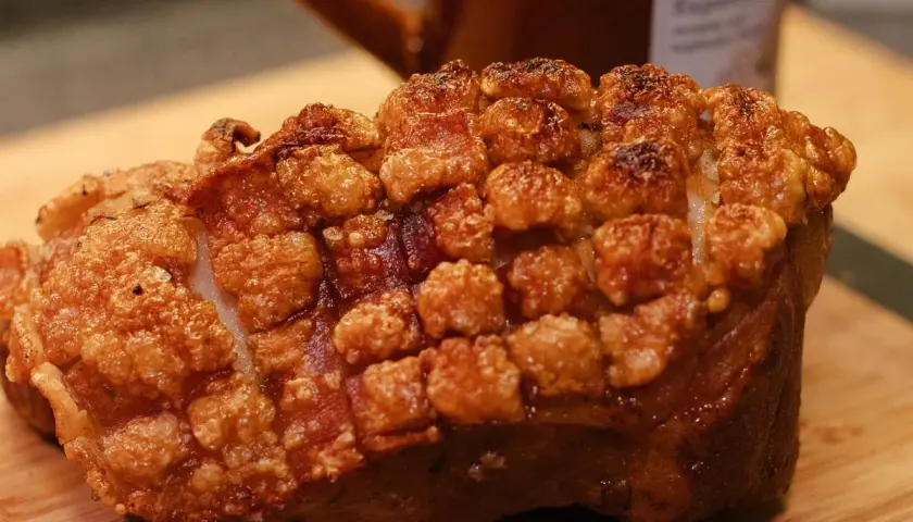 Ein knuspriger, ofenfrischer Schweinebraten mit goldbrauner Kruste liegt auf einem Holzbrett.