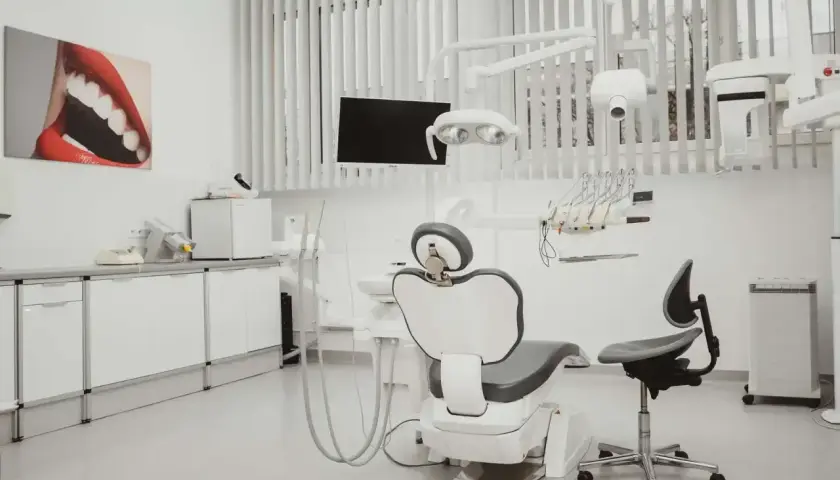 Nowoczesny gabinet stomatologiczny i ortodontyczny. Biały fotel dentystyczny, lampa, wiszące narzędzia i obraz z uśmiechem.