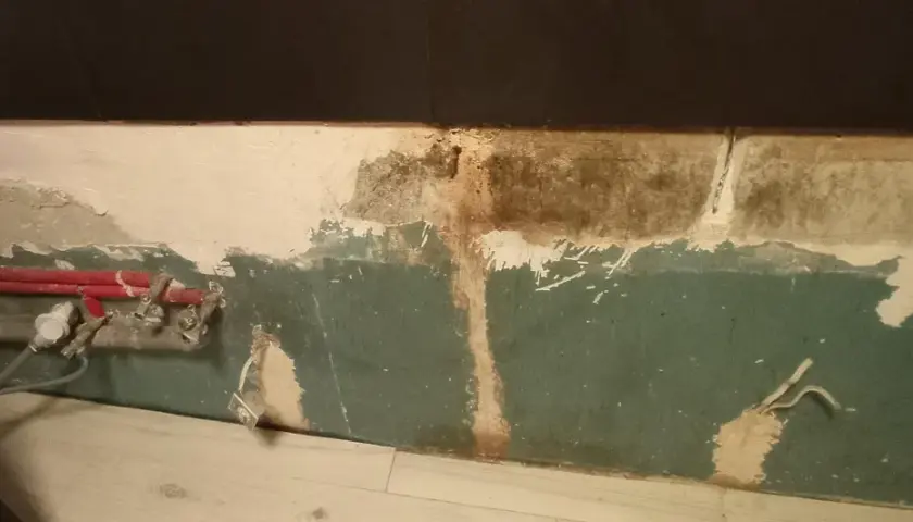 Preparazione per carteggiare muro per imbiancare: tubi rossi e impianto a vista, intonaco scrostato e macchie.