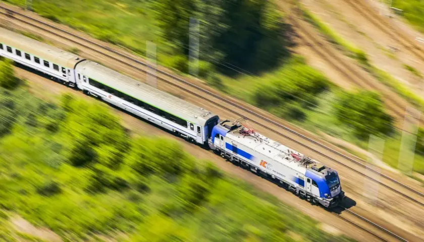 Pociąg PKP Intercity pędzi przez zielone krajobrazy. Szybko kupisz bilet na podróż przez aplikację do zakupu biletów PKP.