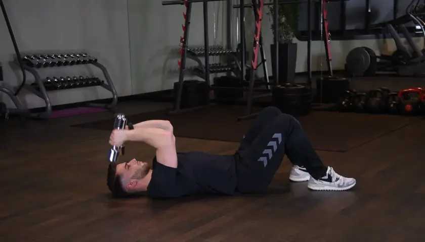 Mężczyzna wykonuje francuskie wyciskanie hantli leżąc na podłodze. Ćwiczenie na triceps.
