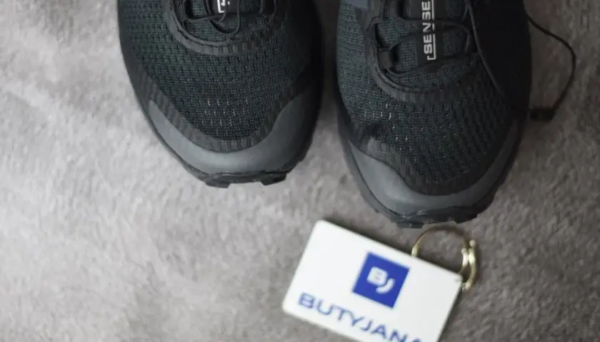 Czarne buty Salomon, model Sense Ride, z metką "BUTYJANA". Salomon to znana firma produkująca odzież i obuwie sportowe.
