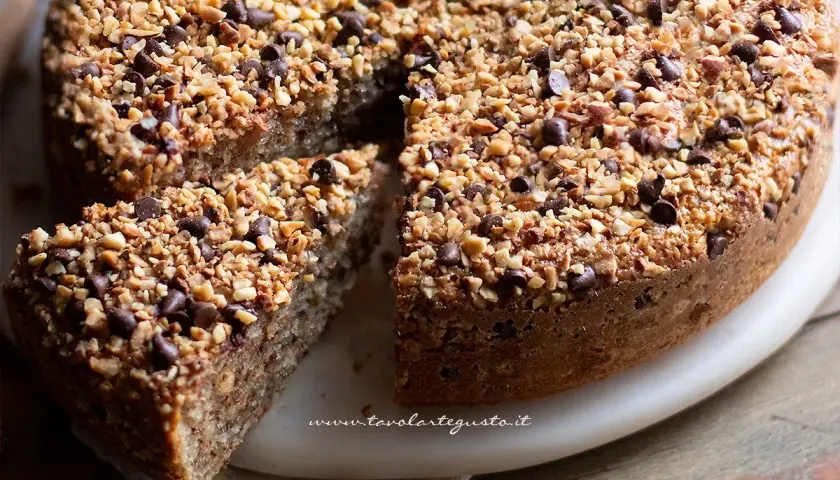 Una deliziosa torta di nocciole, ricoperta di granella di nocciole e gocce di cioccolato, con una fetta tagliata.