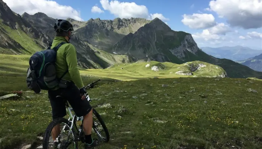 Rowerzysta w zielonej bluzie i kasku z plecakiem na plecach podziwia alpejski krajobraz. Idealny plecak na rower na taką wyprawę.