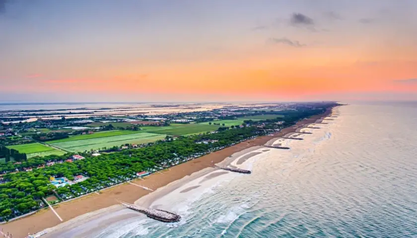 Alba sul mare veneto, con la spiaggia dorata, pineta rigogliosa e lagune all'orizzonte.
