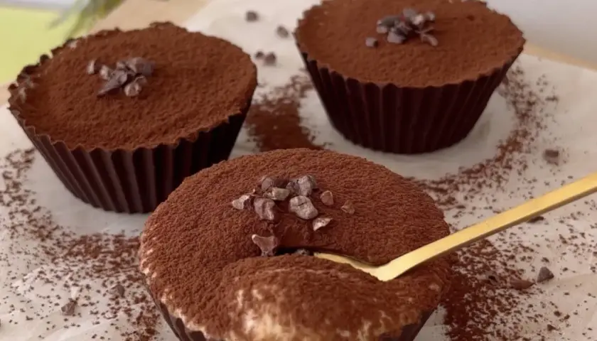 Delicioso postre con ricota, cubierto de cacao y trocitos de chocolate. Una cuchara dorada se hunde en uno de ellos.