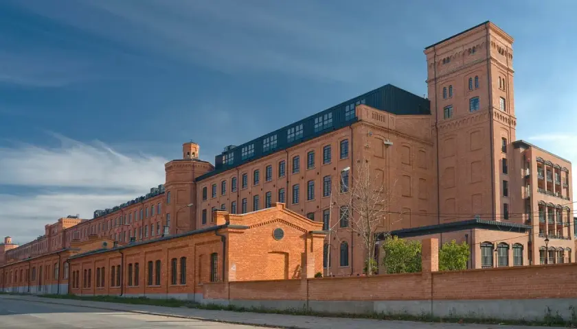 Dawny księży młyn w Łodzi, ceglany kompleks przemysłowy z wieżą, pod błękitnym niebem.