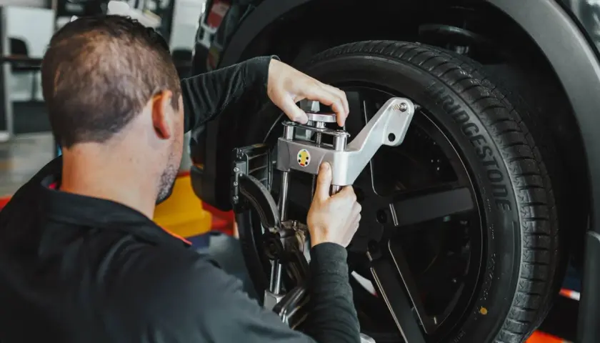 Mecánico ajusta un sensor en la rueda de un coche. Averigua cuanto cuesta alinear un coche para un manejo seguro.