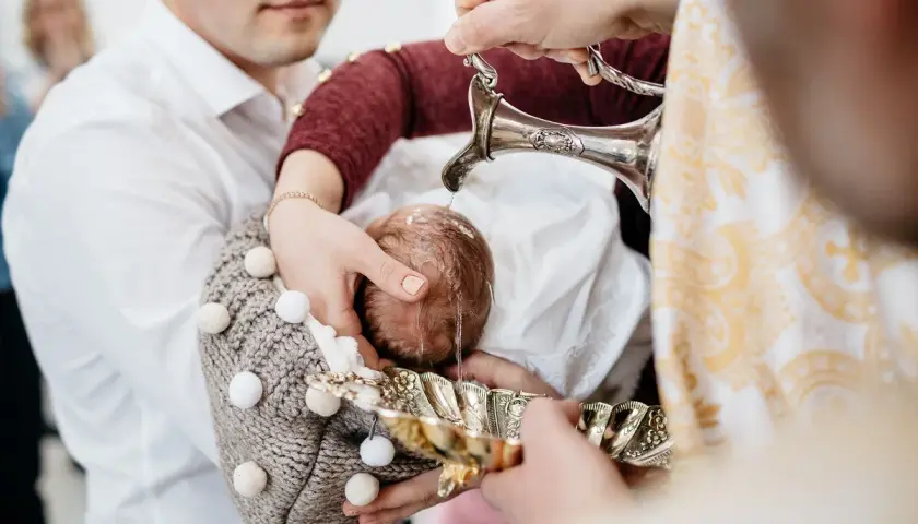 Woda święcona spływa na główkę niemowlęcia, rozpoczynając uroczysty obrzęd chrztu.