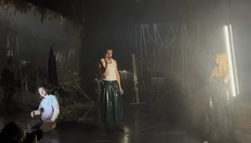 Trzej aktorzy na scenie, jeden klęczy, drugi stoi w błyszczącej spódnicy, trzecia w połyskującej sukni. Scenografia sugeruje **epic the musical**.