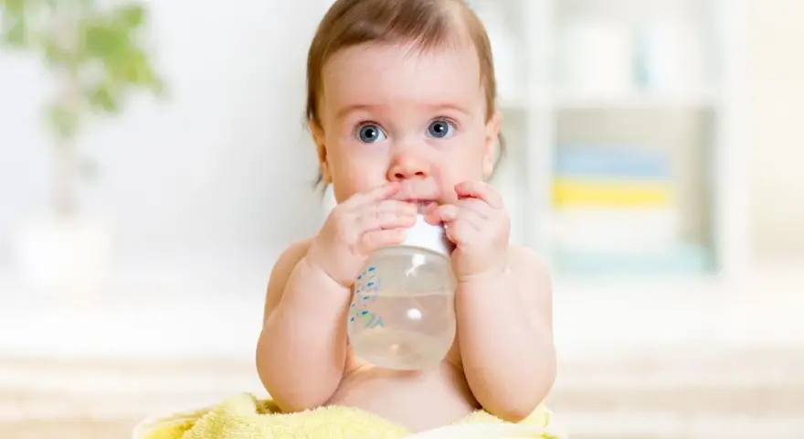 Ein süßes Baby mit blauen Augen hält eine Flasche und trinkt. Es scheint, als ob dieses Baby zu viel trinkt, aber es genießt jeden Schluck.