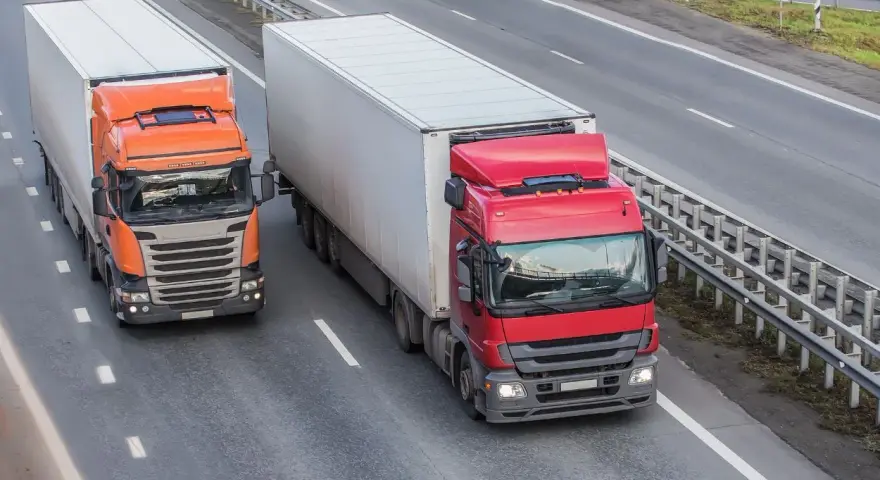 Dwa ciężkie tiry na autostradzie. Czerwony i pomarańczowy, każdy z dużą naczepą. Maksymalny nacisk na oś naczepy to klucz do bezpiecznego transportu.